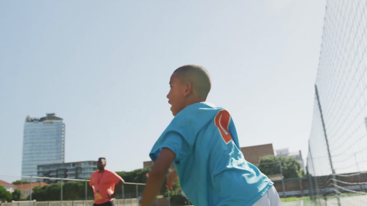 niño de fútbol afroamericano en azul lanzando la pelota en un día soleado