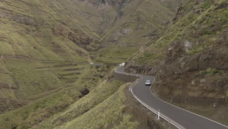 Drone-shot-of-a-car-driving-through-a-curvy-road-in-a-canyon-with-mountains