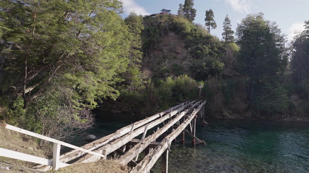 Un antico ponte di legno si estende sulle acque limpide del fiume Correntoso, circondato da una fitta vegetazione. Ideale per progetti di architettura rustica o destinazioni di viaggio remote