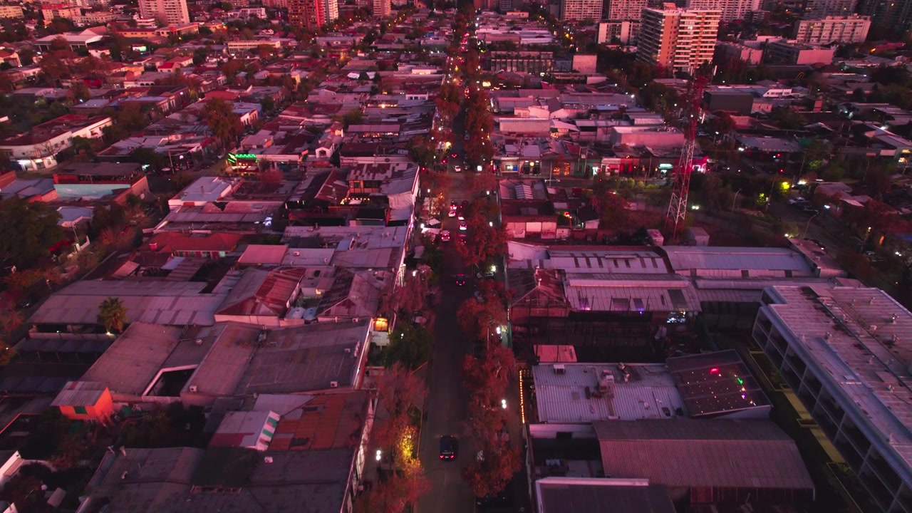 Drone flyover Barrio Italia in Providencia, Traffic on streets with buildings colored by Sunset Lights, Chile