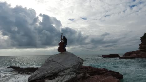 hombre tocando el contrabajo en una roca junto al mar