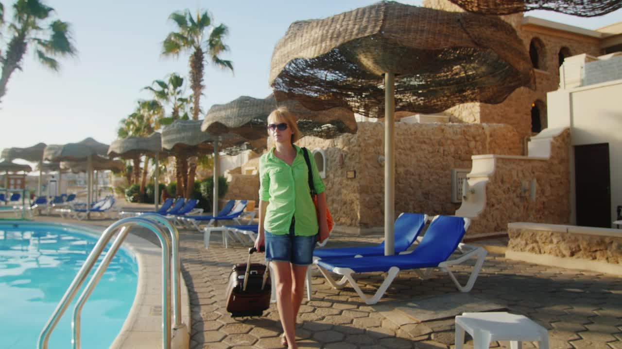 съемка стедикамом женщины с дорожной сумкой, идущей по зоне отдыха вдоль бассейна
