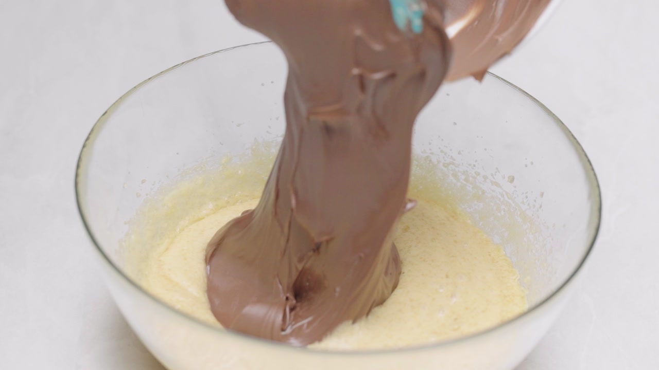 Close up of adding chocolate mixture into batter in bowl using spatula during baking preparation