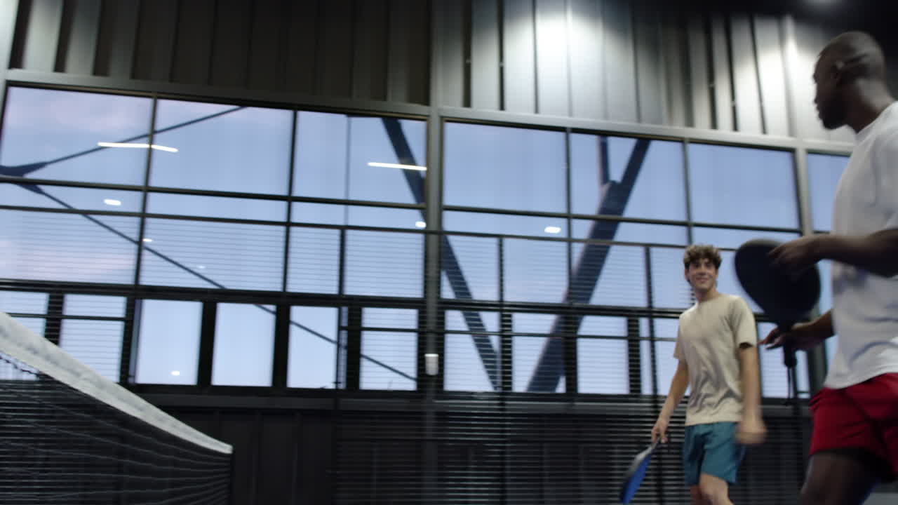 Two diverse men playing padel tennis on indoor court, focused and ready for action