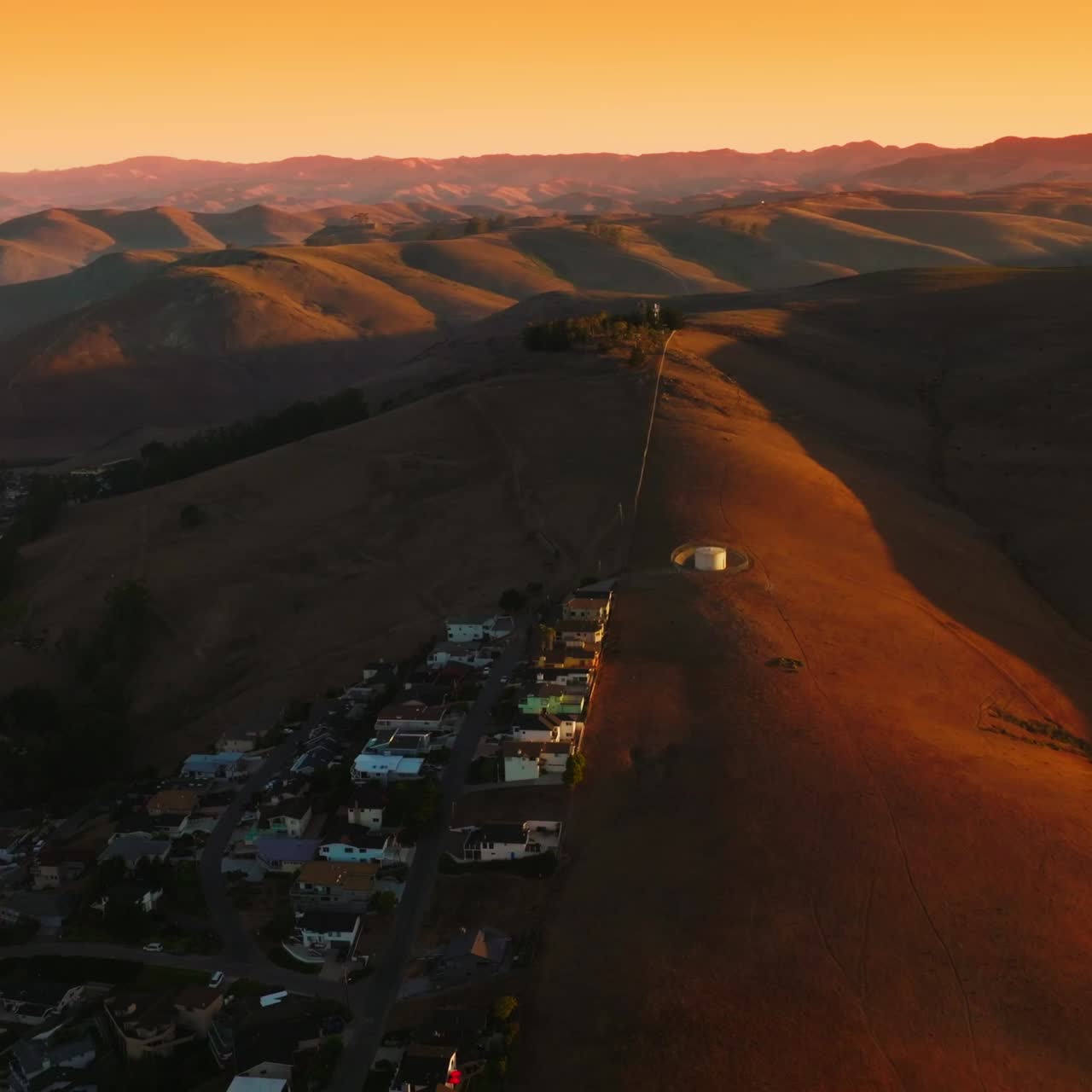 Lovely cozy city at the foot of the mountains. Stunning panorama of bare hills in the beams of setting sun. Aerial view