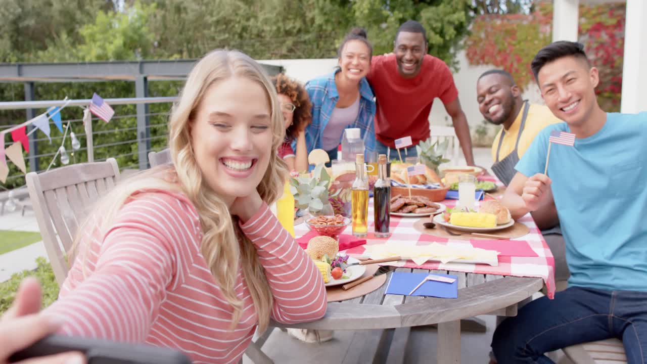Un felice gruppo eterogeneo di amici che si scattano un selfie a tavola in giardino, al rallentatore.