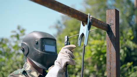 builder welds metal plank fixed with clamp to fence pole