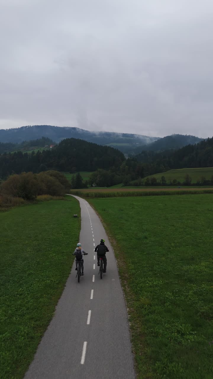 Couple faisant du vélo et conduisant des vélos électriques sur une piste cyclable à la campagne le long d’une rivière, vue aérienne verticale