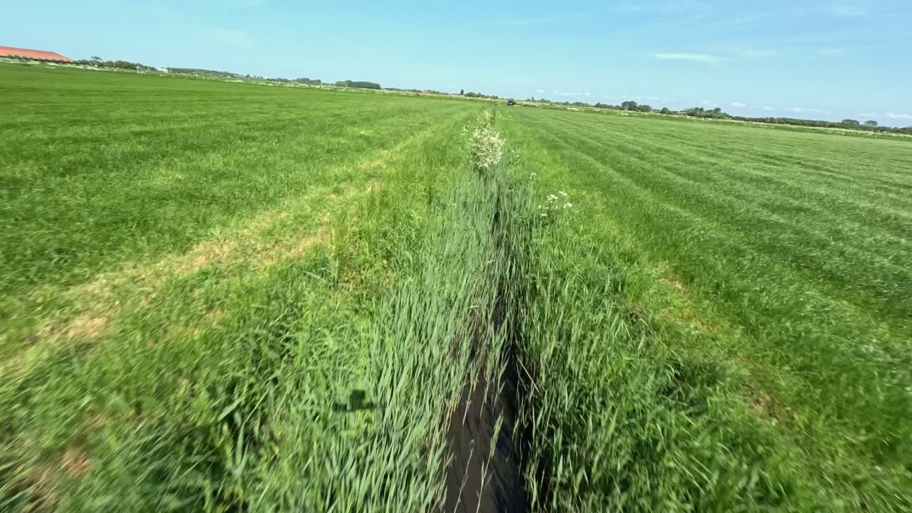 drone fpv volando bajo por encima de una pequeña zanja entre campos de hierba en los países bajos