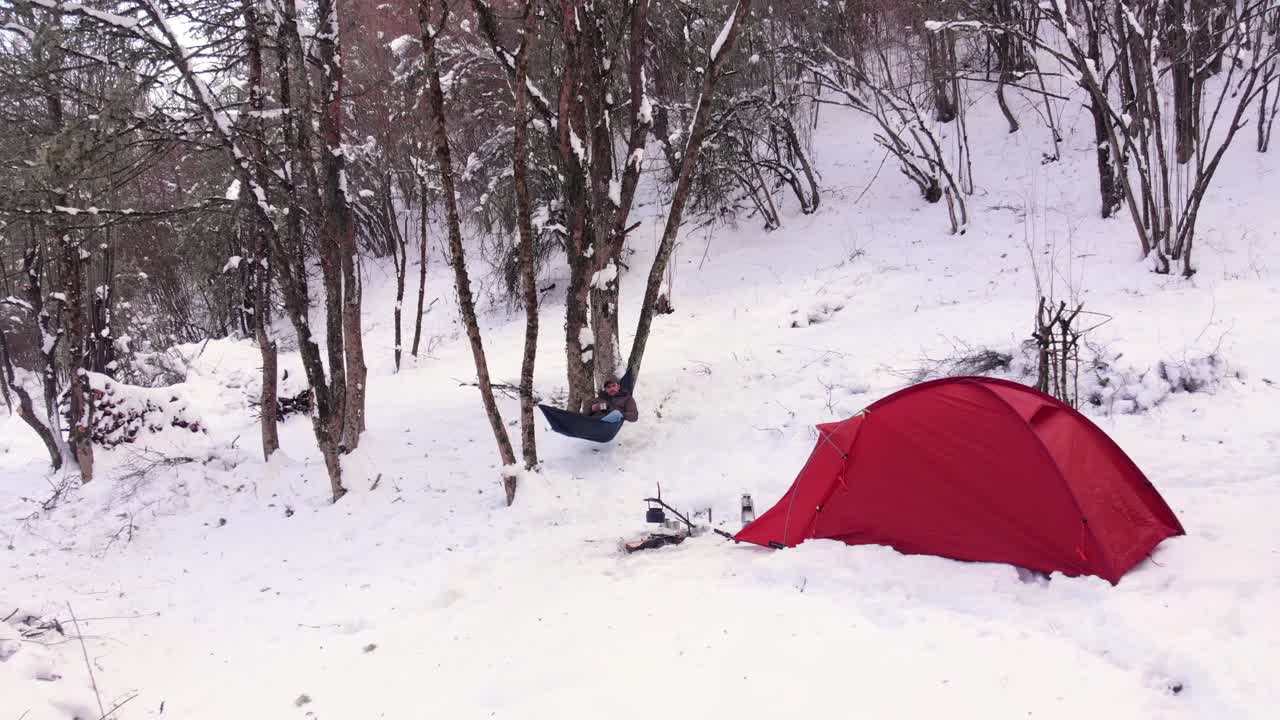 겨울 캠프에서 텐트 근처에서 눈을 즐기는 해먹에서 스윙하는 남자