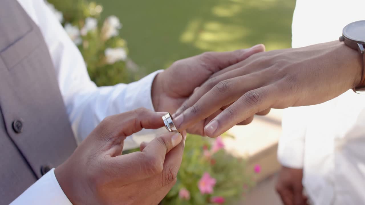 Midsection of african american gay male couple exchanging wedding rings, slow motion