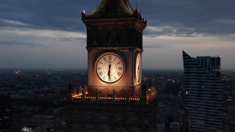 Orbit-shot-around-illuminated-large-tower-clock-on-top-of-Palace-of-Culture-and-Science.-Panning-evening-cityscape-in-background.-Warsaw,-Poland