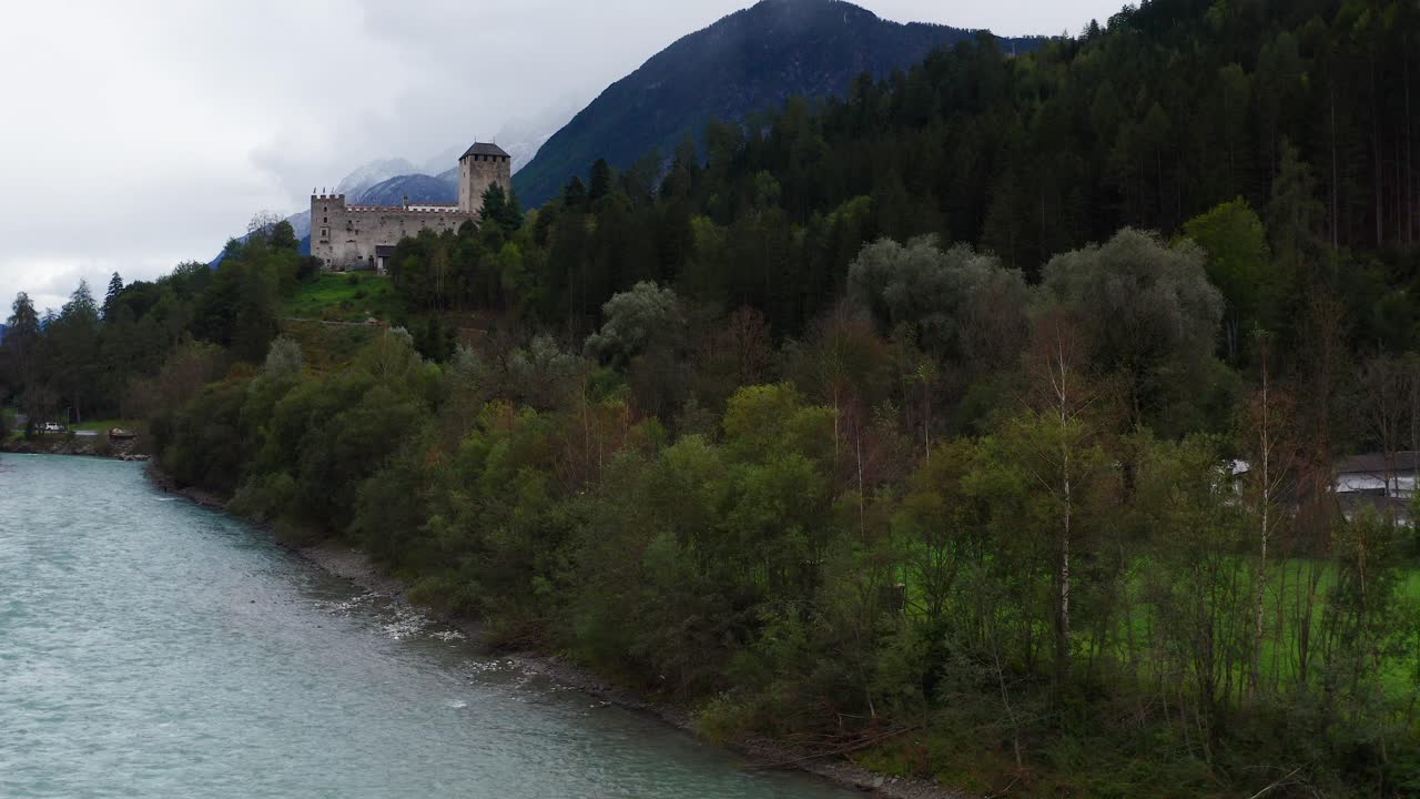 Ripresa aerea ascendente attraverso gli alberi accanto al fiume Isel con vista sul Castello di Bruck in Austria