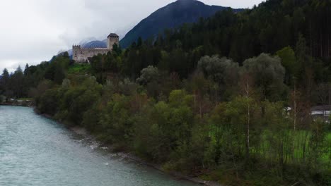aerial ascending through trees beside river isel with view of castle bruck in austria