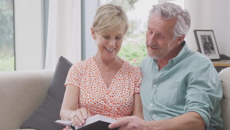 Senior-Retired-Couple-Sitting-On-Sofa-At-Home-Enjoying-Looking-Through-Family-Photo-Album