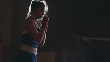 Professional-beautiful-female-boxer-shoots-off-conducting-a-shadow-fight-in-a-dark-hall-room-in-slow-motion-in-blue-clothes-and-red-bandages-on-her-wrists.-steadicam-shot