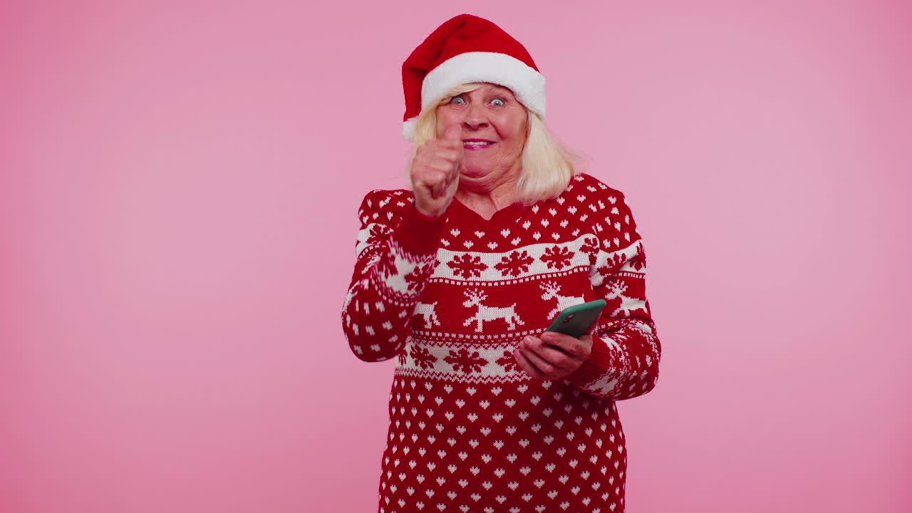 abuela en suéter de navidad mirando pantalla de teléfono inteligente sinceramente regocijándose ganar éxito suerte