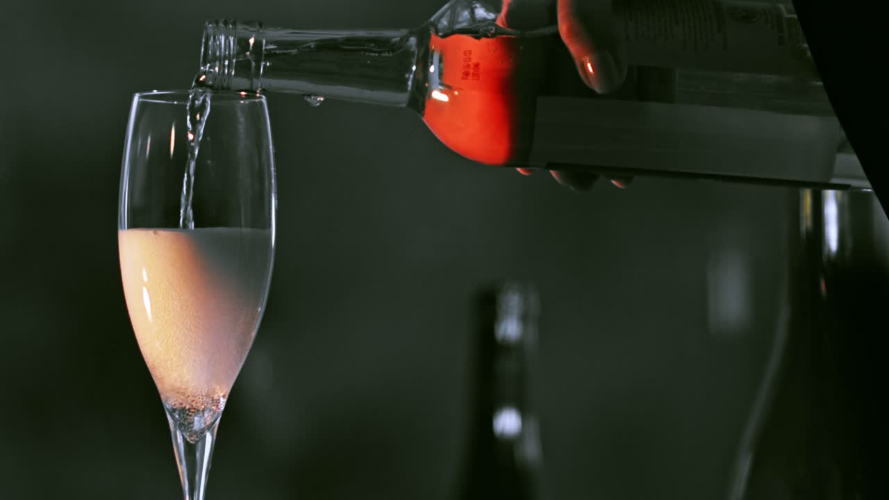 병에서 나온 분홍색 스파클링 로제 와인으로 투명한 유리 플루트를 절반 채우는 것