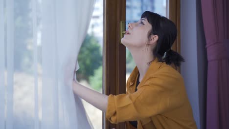 The-young-woman-opens-the-closed-curtains-in-her-house.