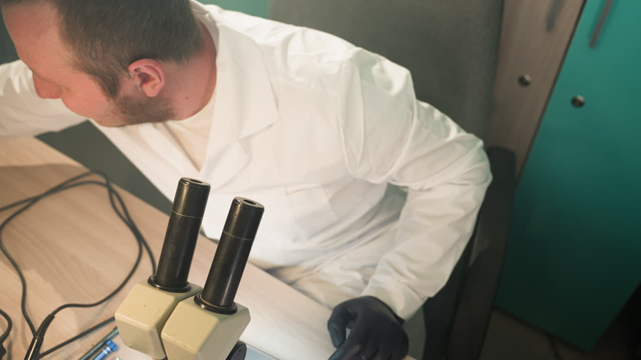 A close-up view of a technician in a lab coat, focused on inspecting electronic components through a microscope, as he get soldering wire from the other side