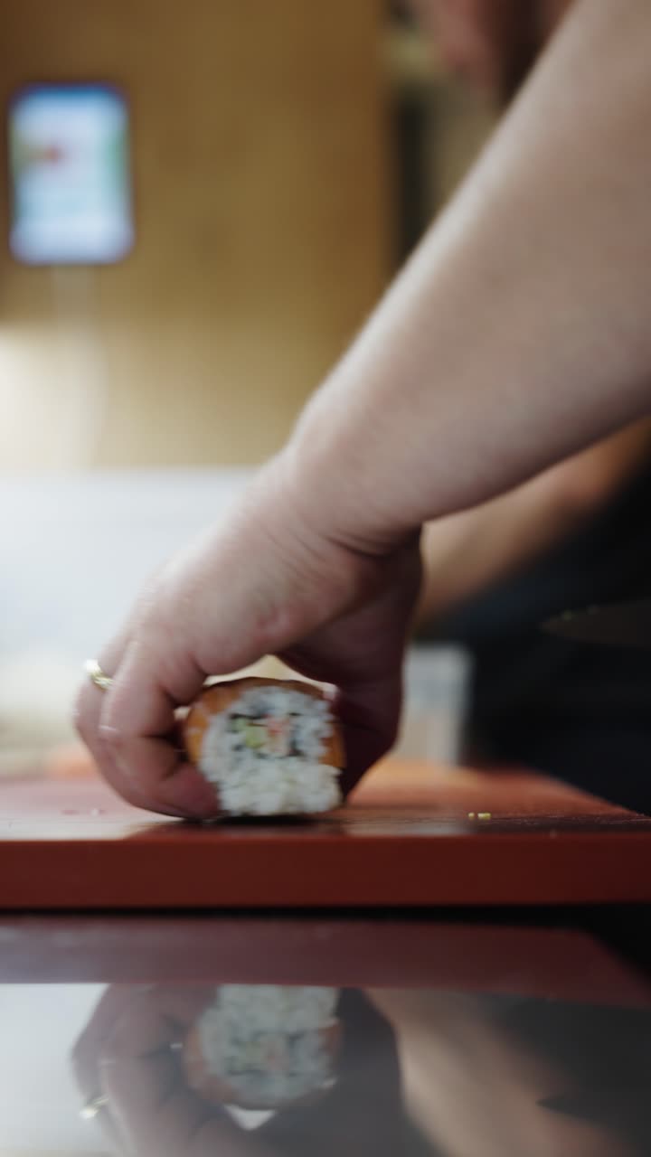 Vertical view of hand hold and cut with knife uramaki sushi with salmon in top