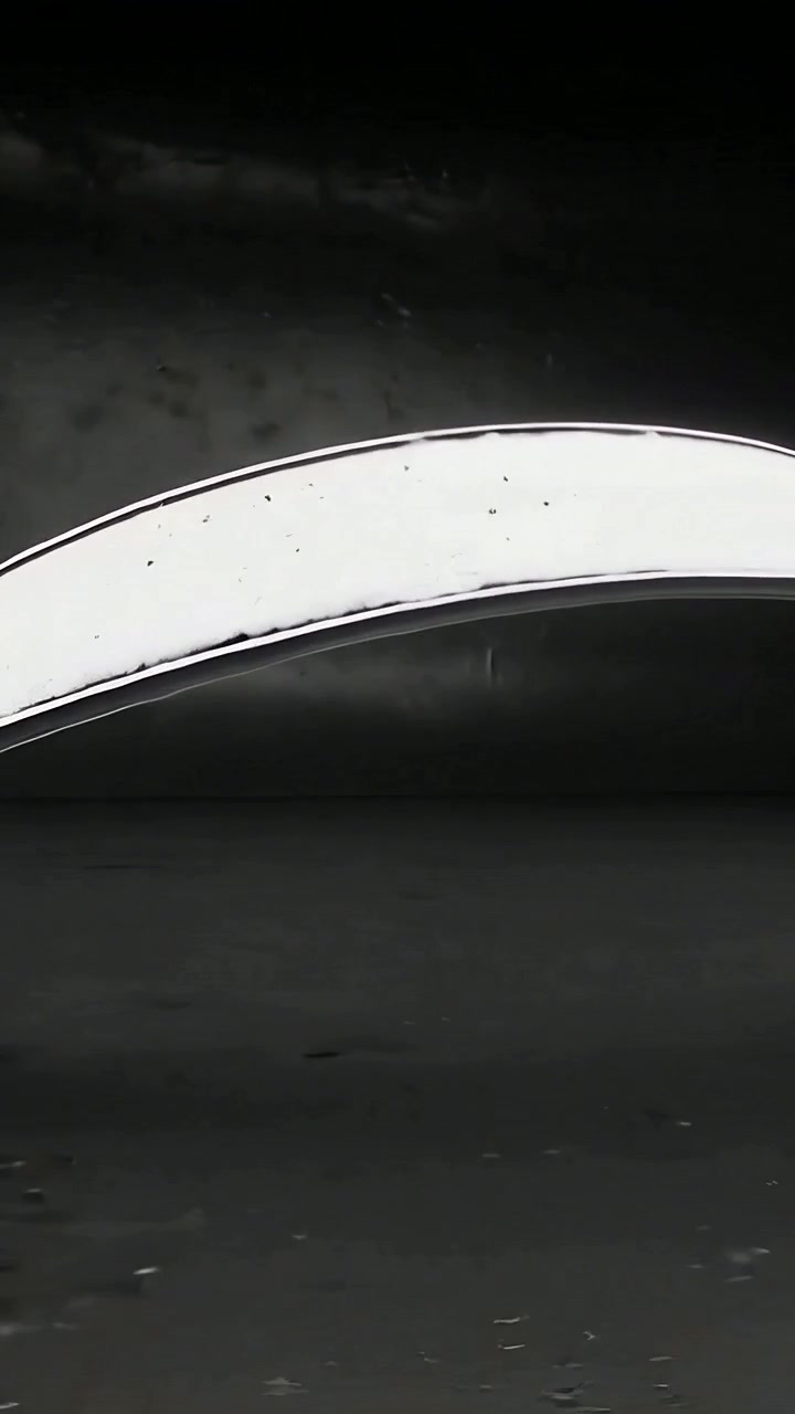 Vertical video: Sliding shiny spoon after offscreen push across black table, showing phone fragment