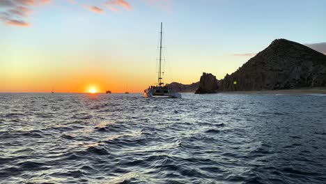 Following-luxury-yacht-sailing-towards-Cabo,-mexico-shoreline-on-sunset-skyline