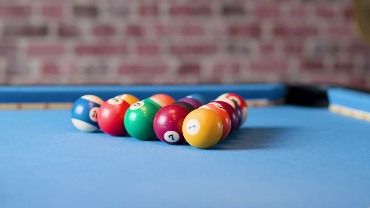 Colorful billiard balls scatter rapidly across blue felt table, shallow focus, brick wall background