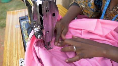 close up slow motion shot from above of an african womans hands as she sews clothing with a tailoring machine