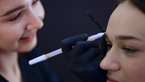 caucasian female beautician drawing line above the eyebrow. microblading, micropigmentation eyebrows work flow in a beauty salon. extreme close up.