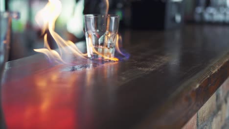 barman prepares a cocktail in a glass and sets it on fire on bar counter. trasparent liqiud of alcohol in glass on fire