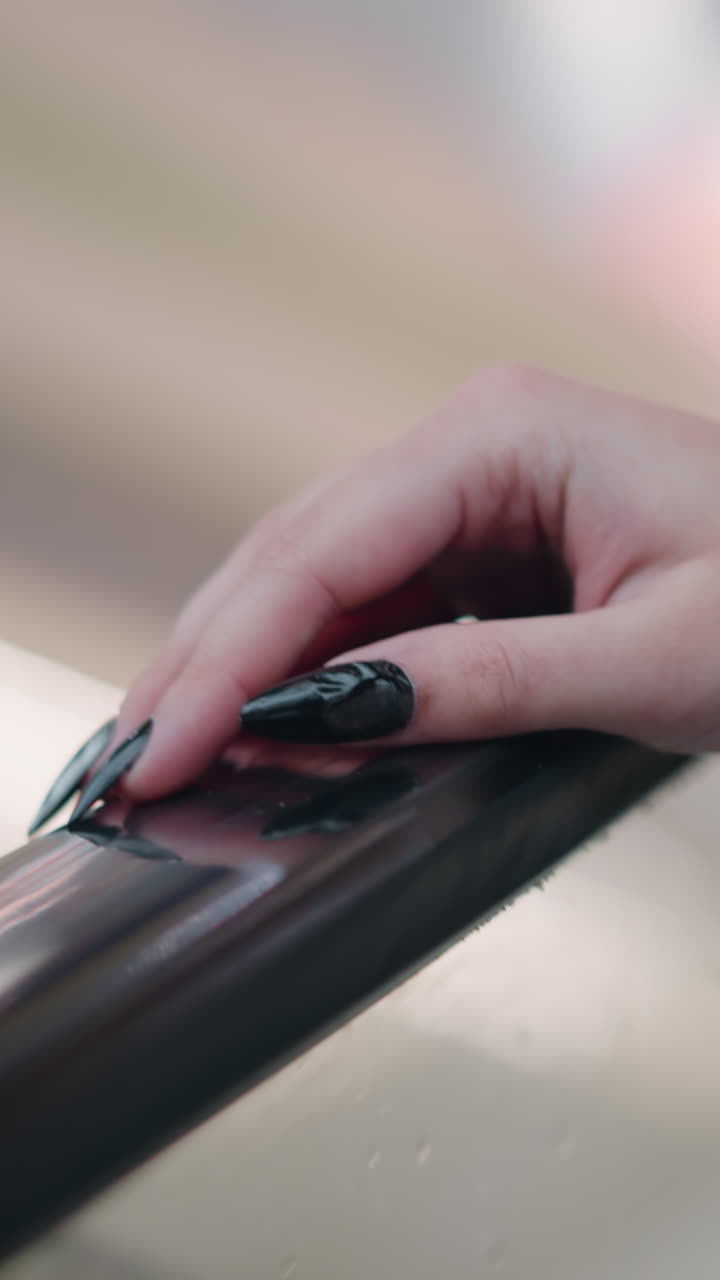 긴 검은색 은 손을 가진 여자의 손이 올라가는 동안 에스컬레이터 레일에 누워있는 클로즈업, 멋진 반사와 함께 현대적인 실내 설정에서 부드러운 보케 조명을 특징으로하는 배경