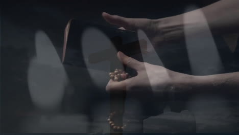 animation of burning candles over hands holding bible and rosary on black background