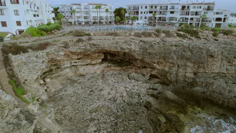 Drohnenclip,-Der-Einen-Felsigen-Kinostrand-In-Der-Nähe-Eines-Hotelresorts-Auf-Mallorca,-Spanien,-Zeigt