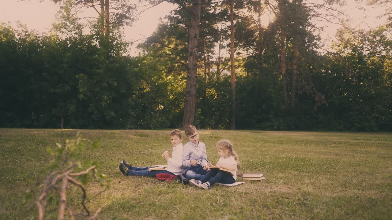 Skolpojkar med en liten flicka äter lunch på gräset i en park.