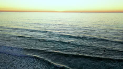 Aerial-shot-of-Scripps-Pier-at-sunset-over-the-ocean-with-surfers-in-San-Diego,-California