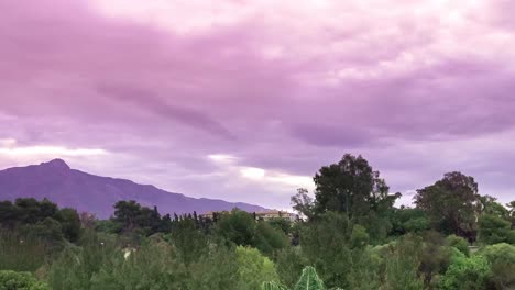 4k siniestro lapso de tiempo parpadeante de nubes púrpuras moviéndose sobre árboles y montañas, filmado en marbella, málaga, españa