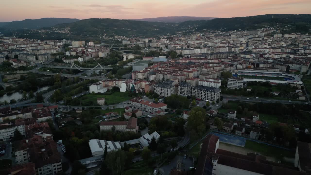 Drone descends over grand establishing view of Ourense Spain at sunset