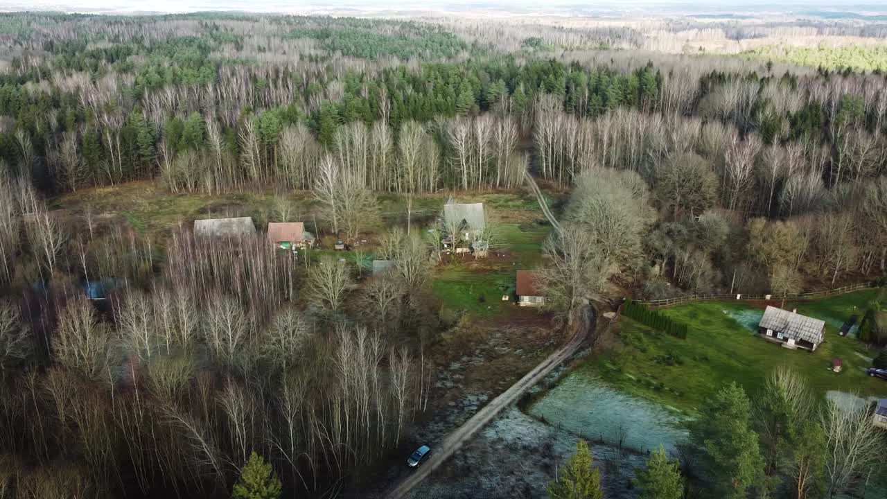 Flygbild över liten by omgiven av tät skog tidig vinter medan trädkronorna är frusna