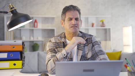 mature home office worker looking at laptop with worry and despair sees bad news.