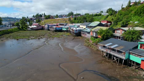 Coloridas-Casas-Sobre-Pilotes-En-La-Isla-De-Chiloé-Con-Marea-Baja-Exponiendo-El-Fondo-Marino,-Día-Soleado,-Vista-Aérea