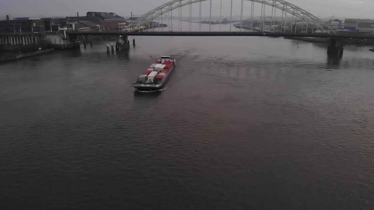 Cargo vessel loaded with a lot of containers sailing on the dutch river Noord passing a bascule bridge. Slowmotion drone truck shot