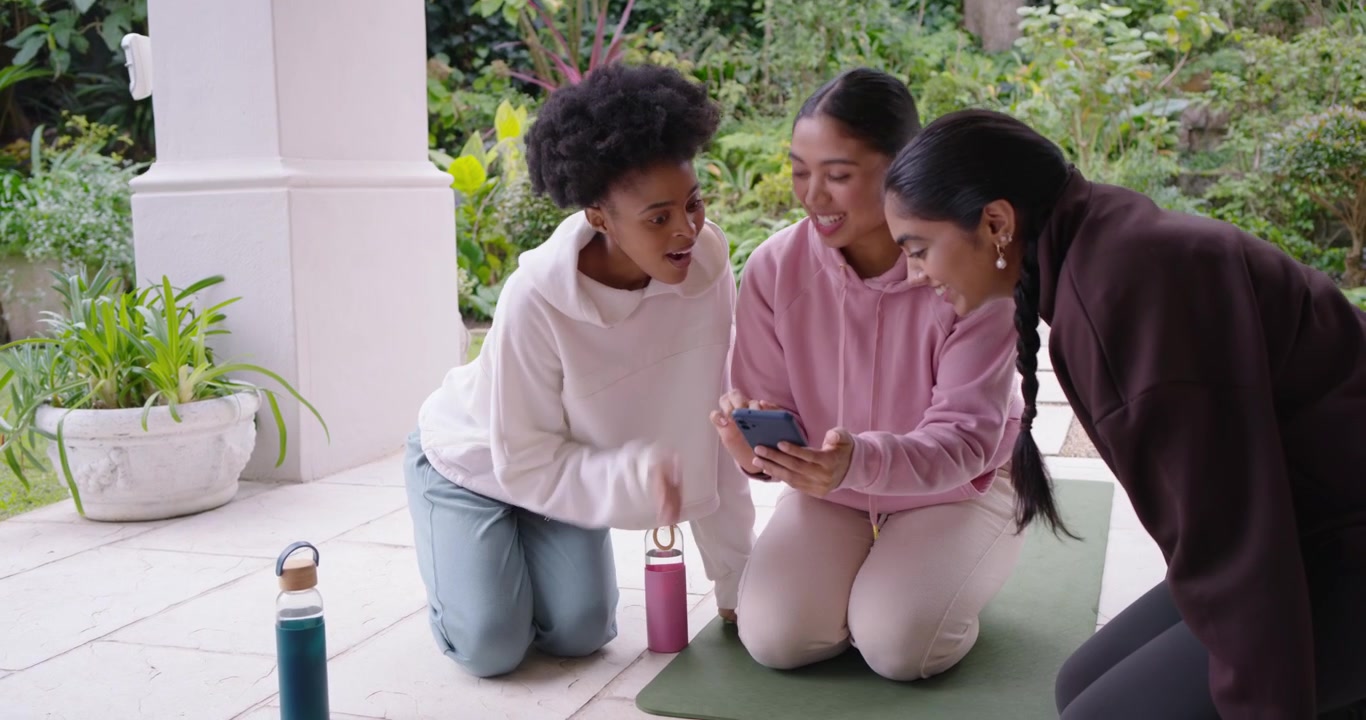 Diverse women friends ending meditation central woman grabbing phone and sharing content on patio