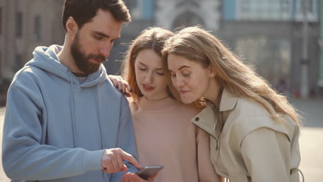 a group of three young friends watching something on the screen of the cell phone