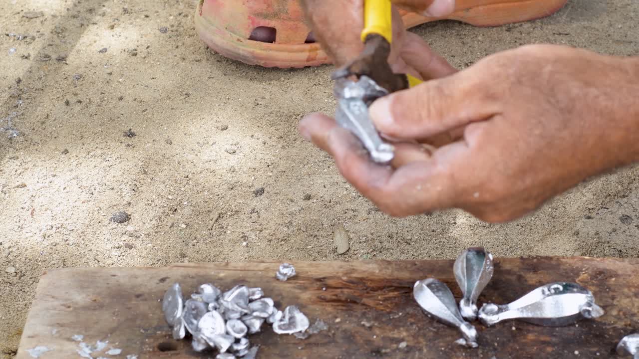 사람의 손은  클리어 도구를 사용하여 시 싱커에서 과도한 폐기물 납을 잘라내고 다시 녹인다.