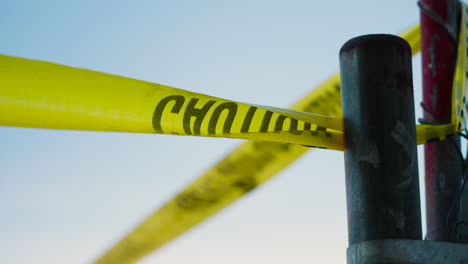 a piece of yellow caution tape tied to a fence outside of a crime scene blowing in the wind