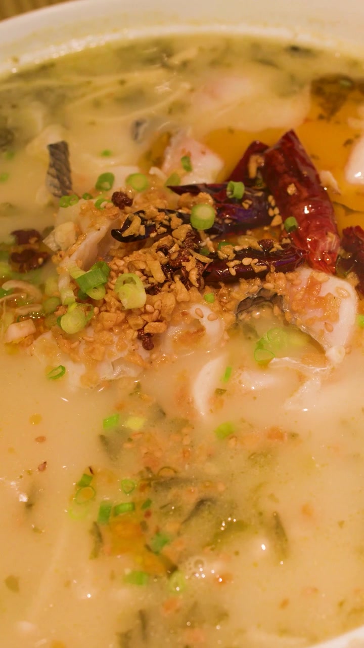 Nærbillede af dampende, krydret fiskesuppe med røde chilier og urter i en hvid skål.