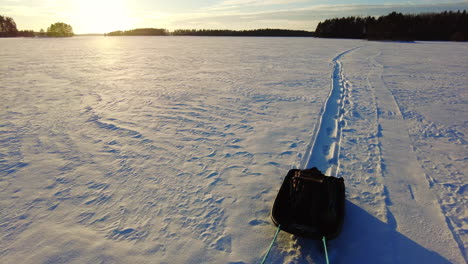 Pov-Caminar-Hacia-Atrás-Y-Arrastrar-El-Trineo-En-Un-Lago-Cubierto-De-Hielo-Nevado-Al-Atardecer-Hora-Dorada