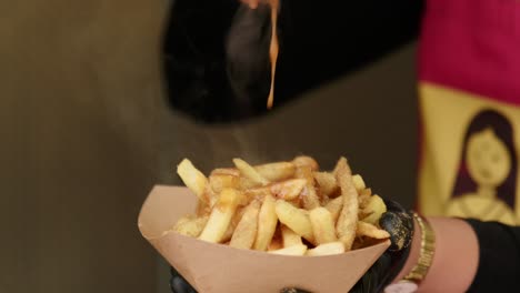 close up of chef pouring hot creamy chilli sauce down on warm crispy french fries at festival inside food truck.