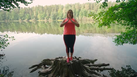 a caucasian woman in sportswear standing on a tree stump and practicing yoga